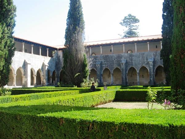 Gothic cloister of Batalha, stone arches among cypresses and green hedges