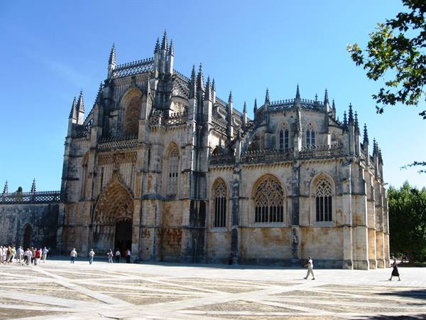 Tourists walk before Batalha Monastery, Gothic stonework under a blue sky