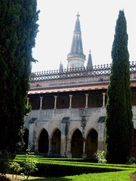 Gothic stone cloister with arches and spire, cypresses and green hedges, Batalha