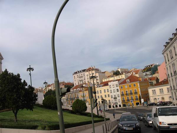 Uphill street in Lisbon, colorful buildings, queued cars, cloudy sky