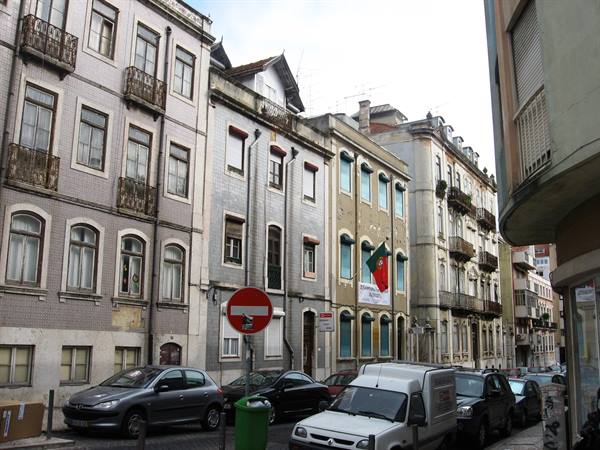 Tiled buildings with Portuguese flag above parked cars and van, Lisbon