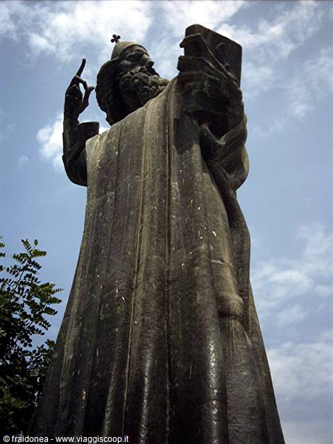 Bronze statue of a blessing bishop against a cloudy sky