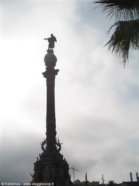 Columbus Monument backlit in Barcelona, with palm tree and cloudy sky