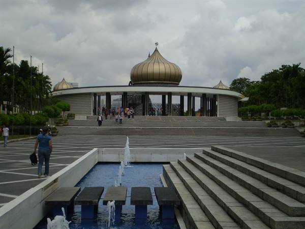 National Monument in Kuala Lumpur, golden dome, fountains and visitors on the steps
