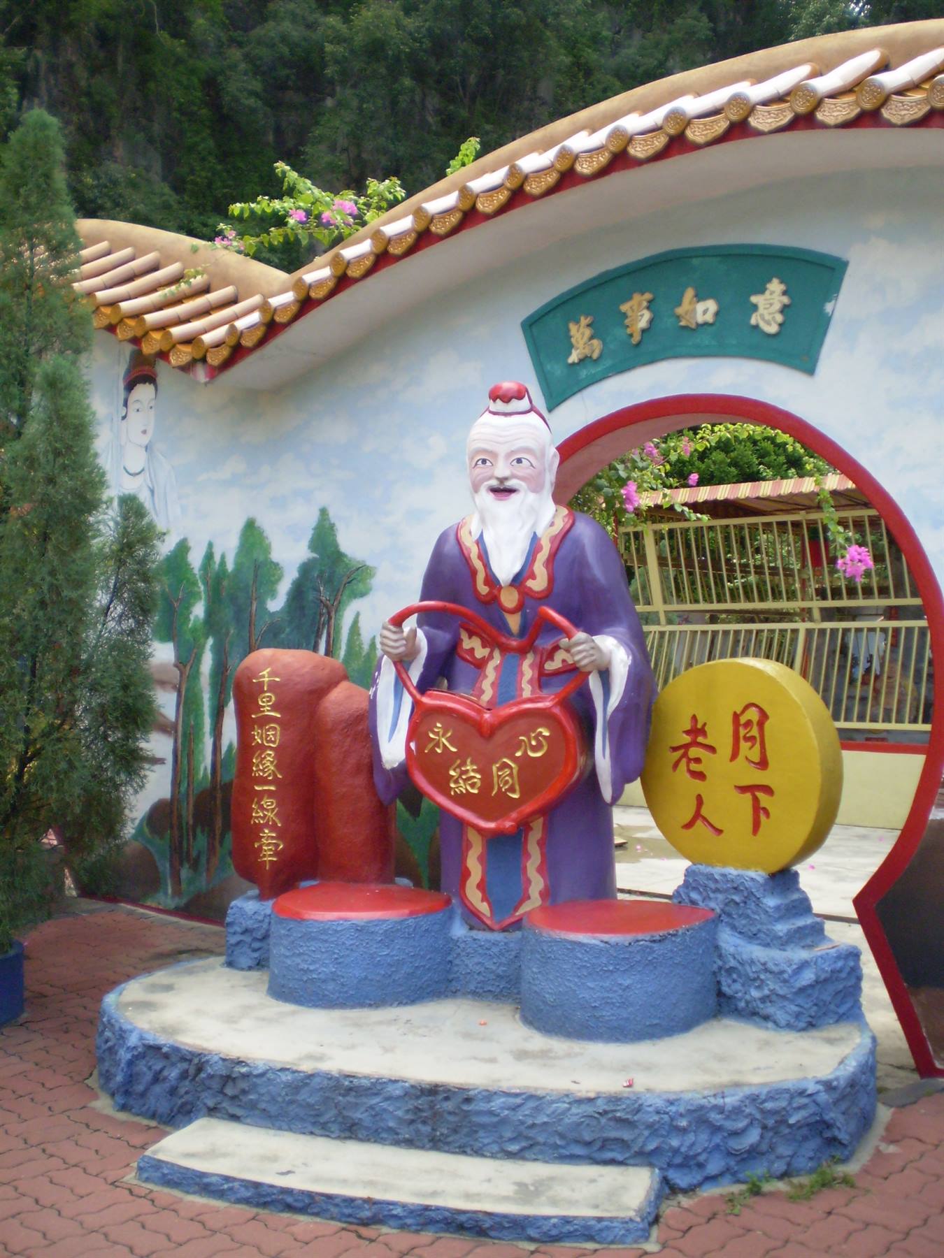 Colorful statue of elderly deity holding red heart before moon gate