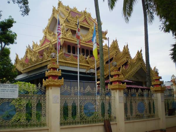 Buddhist temple with golden roof and flags behind ornate fence