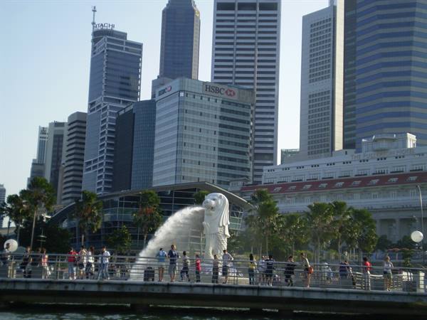 Tourists by the Merlion statue spouting water, Singapore skyscrapers behind