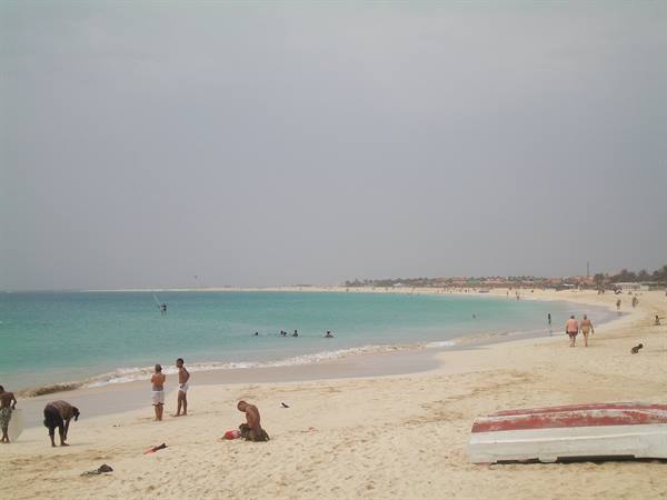 Bathers on pale sand with red boat at Santa Maria, Sal