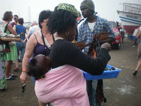 Woman with baby on her back sells necklaces at harbor market