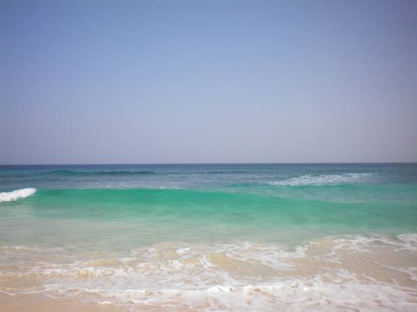 Turquoise wave breaking on pale sand under a blue sky