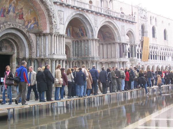 Tourists on walkways across flooded St Mark's Square, Basilica mosaics above