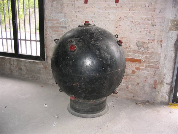 Black metal sphere on cylindrical base inside a brick building