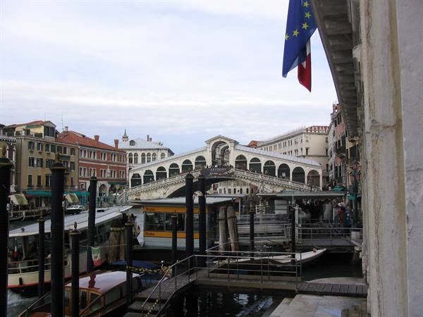 Rialto Bridge in Venice, flags in foreground, boats docked along the Grand Canal
