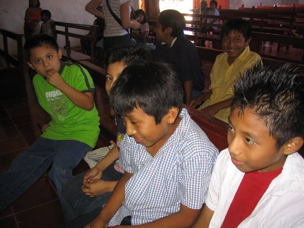 Children sitting on wooden pews, warm light from the back