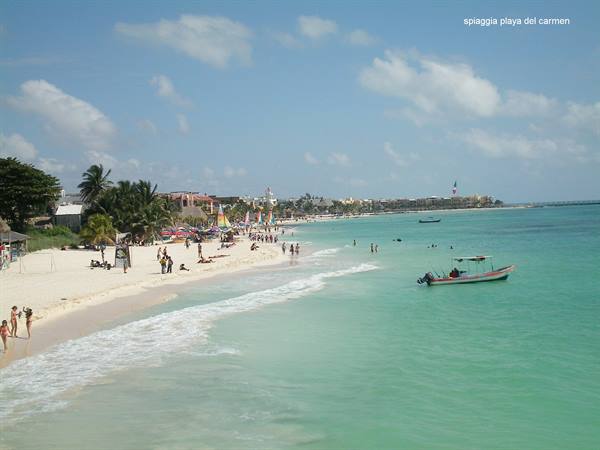 Playa del Carmen beach: fishing boat on turquoise water, swimmers and umbrellas in the sun