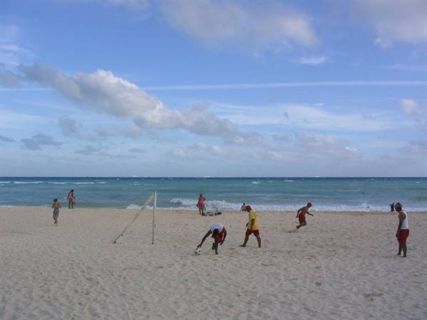 Boys play soccer on the sand in front of the turquoise sea