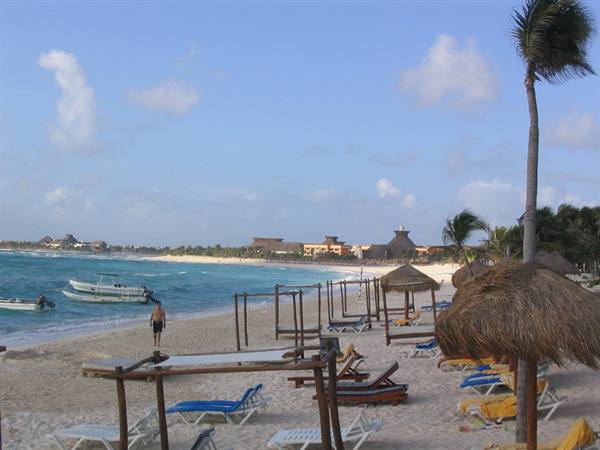 Sandy beach with straw umbrellas, loungers and boats near the shore, Tulum