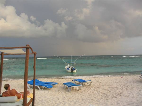 Motorboat anchored offshore, blue loungers on white sand beach under cloudy sky