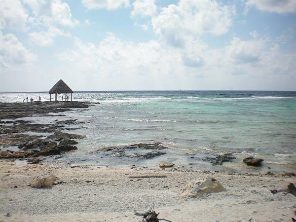 Thatched palapa on limestone rocks, people nearby, turquoise sea and pale sand
