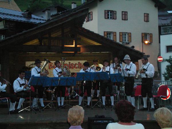 Traditional brass band in folk costume performs under a wooden stage among alpine houses