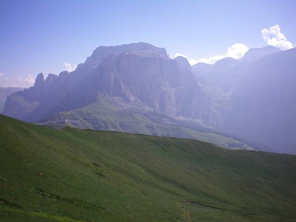 Dolomite massif in haze above a green grassy slope