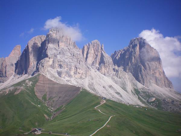 Dolomite peaks above a green meadow with winding path and hut