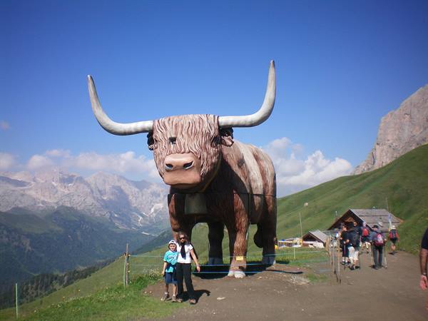 Tourists beside a giant wooden cow statue in the mountains under blue sky