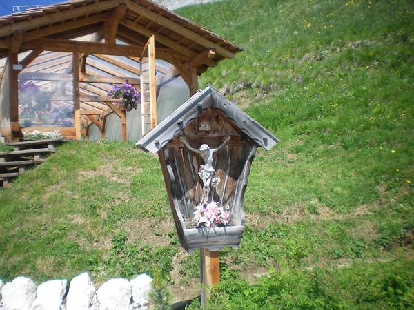 Wooden wayside shrine with crucifix on alpine meadow near wooden hut
