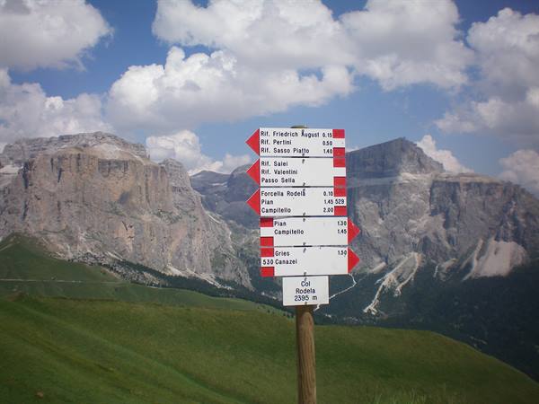 Trail signpost at Col Raiser 2530 m among Dolomite peaks under white clouds