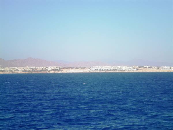 Deep blue sea in front of white coastal hotels, arid mountains behind