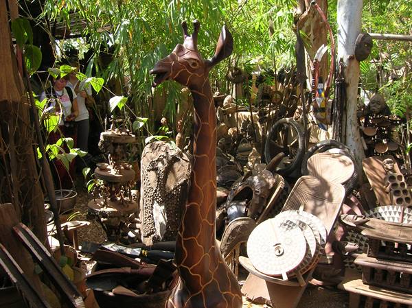 Wooden giraffe sculpture among other handcrafted statues in the shade
