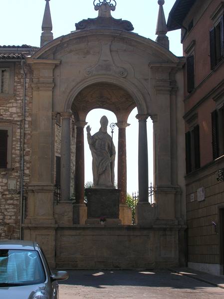 Stone statue of a blessing bishop under a baroque aedicula between old houses