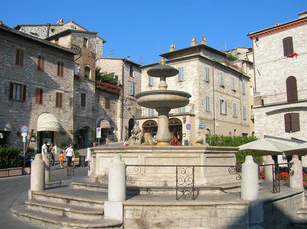 Stone Fountain Maggiore in Assisi, medieval houses, tourists under sunny sky