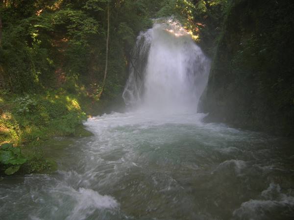 Waterfall between rocks and green vegetation, white water plunging into river