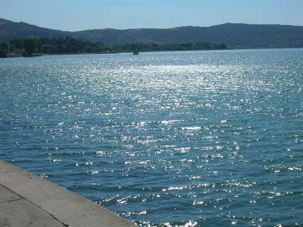 Sparkling lake water by a stone pier, green hills in the background