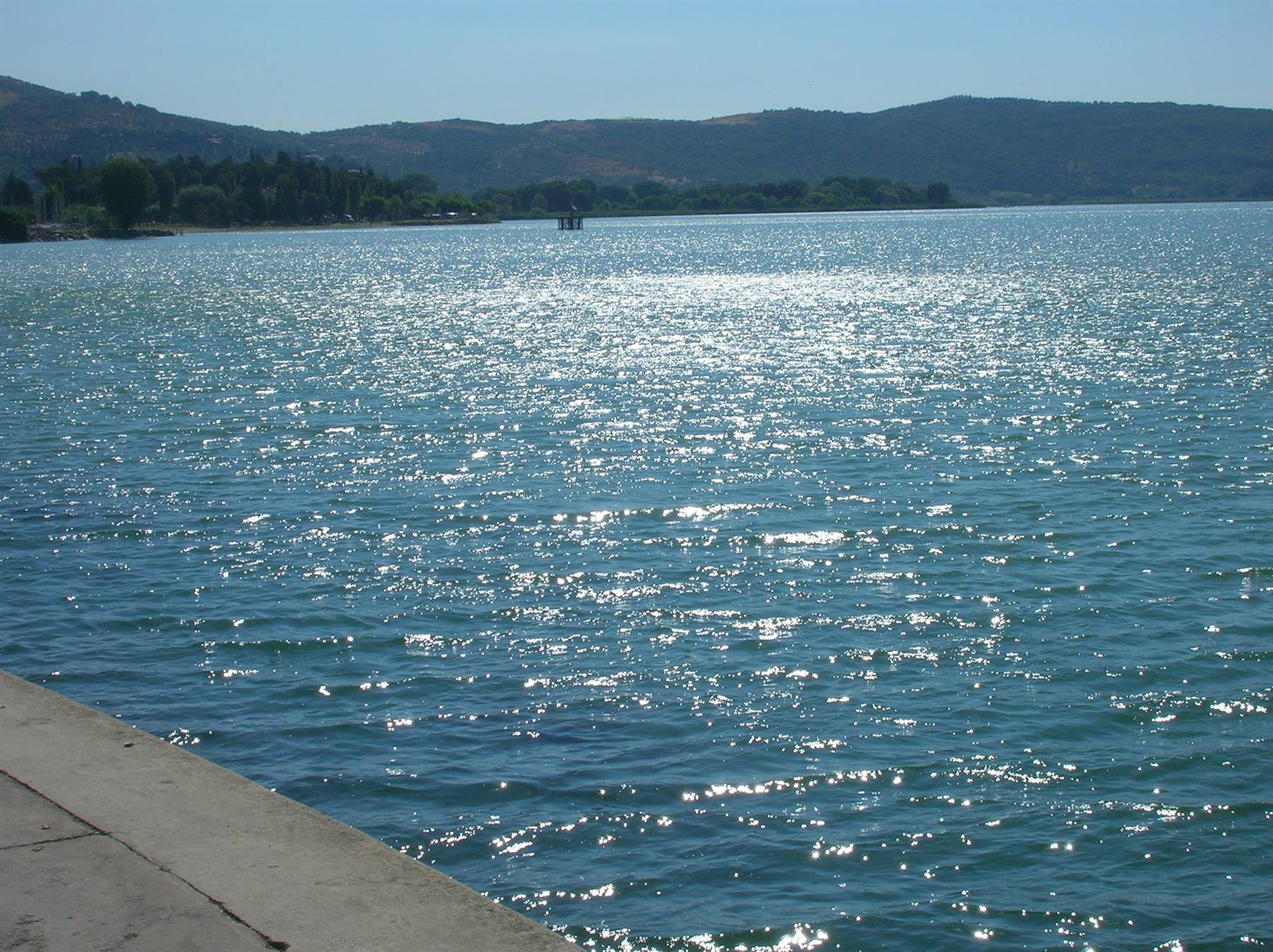 Sparkling lake water by a stone pier, green hills in the background