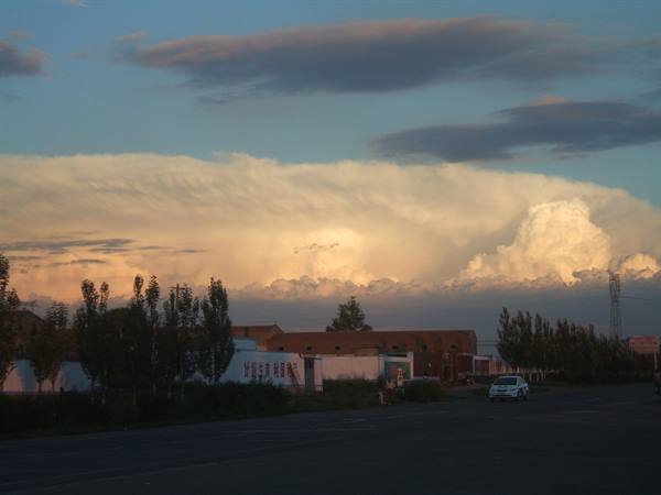 Sunlit clouds over rural houses and road, white car at dusk