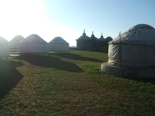 White canvas yurts on green grass, backlit, near Mongolian gers