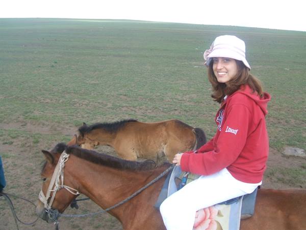 Girl in red hoodie and white hat riding a brown horse on the grassland