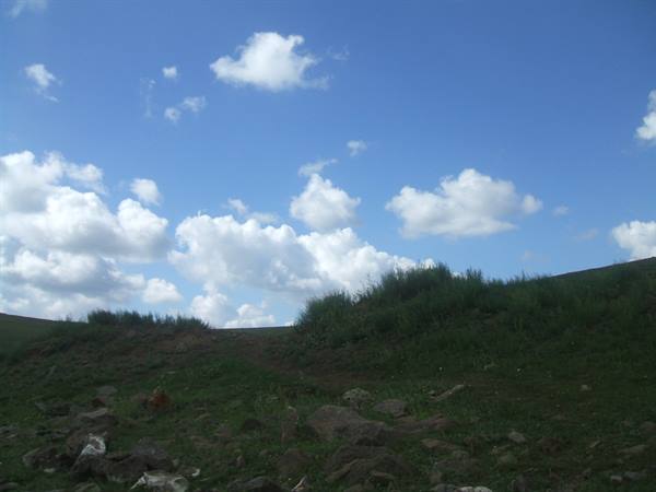 grassy hill with scattered rocks under blue sky and white clouds