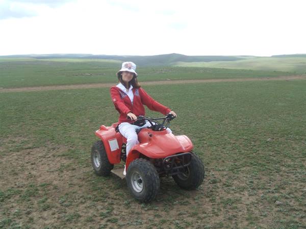 Woman in red jacket and hat riding a red quad bike on grassy steppe