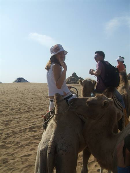 Tourists riding camels across sandy desert dunes under blue sky