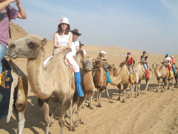 Tourists riding camels across the sandy dunes under bright sunlight