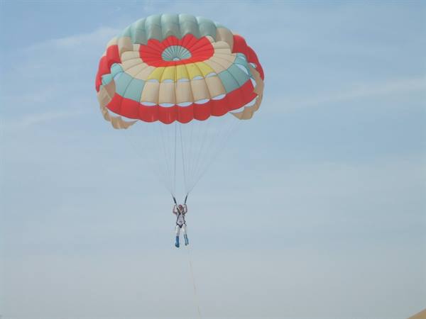 Tourist hanging from a red and turquoise parasail in the blue sky