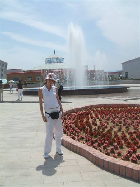 Woman dressed in white poses by fountain and red brick flower bed