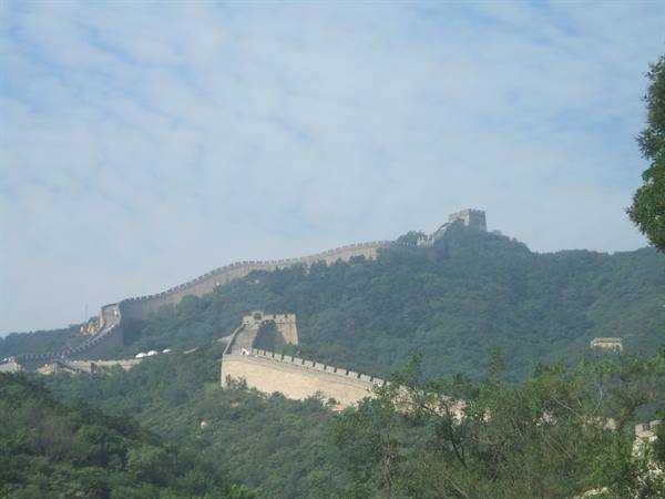 The stone Great Wall climbs between watchtowers on the green hill