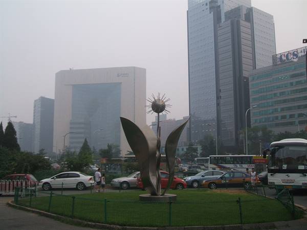 Metal flower sculpture on a busy roundabout among skyscrapers in hazy smog