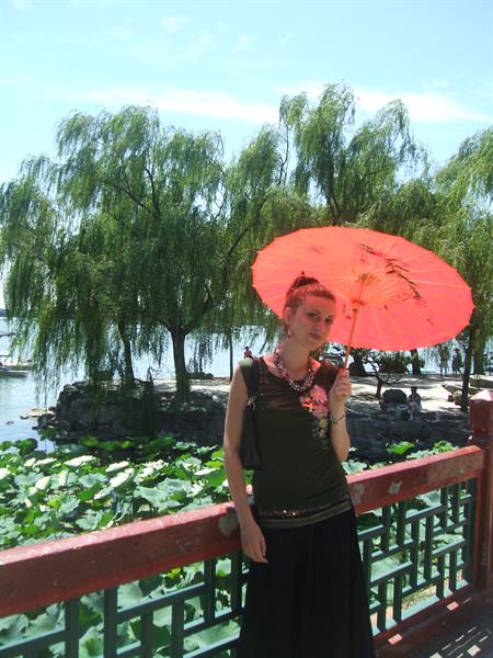 Woman with red paper parasol on red wooden bridge, willow-lined lake