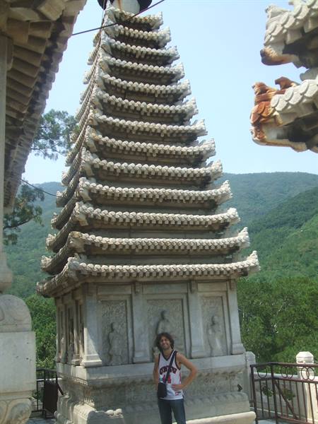 Tourist beside a carved stone pagoda with tiered roofs, green hills behind