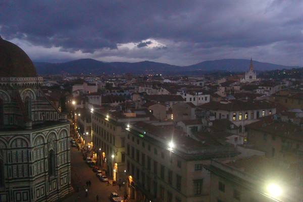 Florence Duomo dome among rooftops and streetlights under cloudy sky
